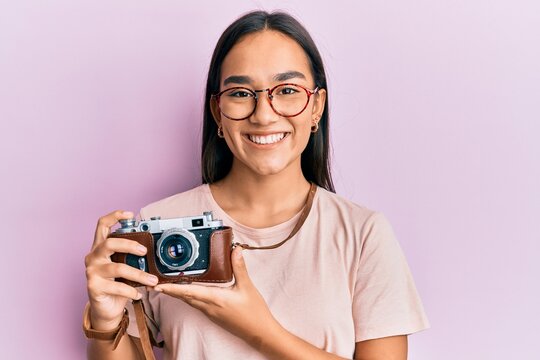 Young asian woman holding vintage camera smiling with a happy and cool smile on face. showing teeth.