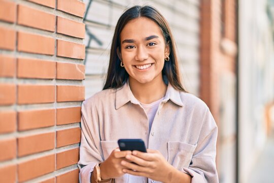 Young latin girl smiling happy using smartphone at the city.