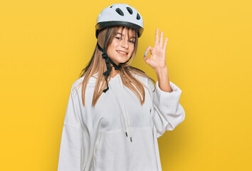 Teenager caucasian girl wearing bike helmet smiling positive doing ok sign with hand and fingers. successful expression.
