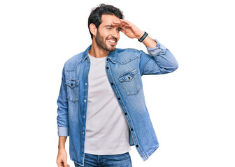 Young hispanic man wearing casual clothes very happy and smiling looking far away with hand over head. searching concept.