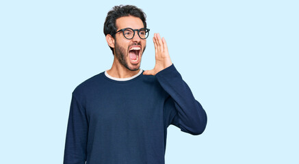 Fototapeta premium Young hispanic man wearing casual clothes and glasses shouting and screaming loud to side with hand on mouth. communication concept.