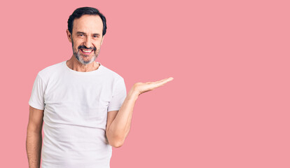 Middle age handsome man wearing casual t-shirt smiling cheerful presenting and pointing with palm of hand looking at the camera.