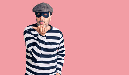 Middle age handsome man wearing burglar mask looking at the camera blowing a kiss with hand on air being lovely and sexy. love expression.