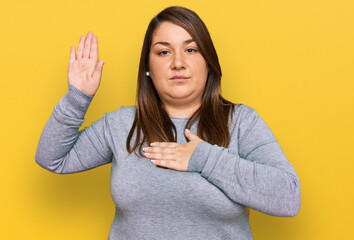 Beautiful brunette plus size woman wearing casual clothes swearing with hand on chest and open...