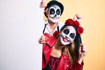Fototapeta na wymiar Couple wearing day of the dead costume holding blank empty banner screaming proud, celebrating victory and success very excited with raised arm