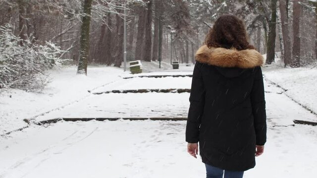 Woman in jacket walking on trail in forest  covered by snow in winter season