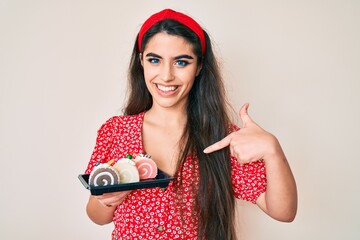 Brunette teenager girl holding cake sweets pointing finger to one self smiling happy and proud