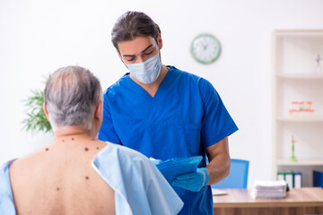 Fototapeta premium Old man visiting young male doctor dermatologist