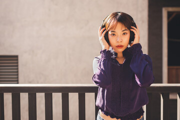 Happy young asian woman listening to music with headphones and looking at camera on the street.