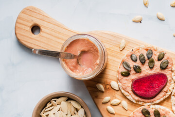Hummus in jar by Crispy puffed rice cakes on table hummus spread and tomato and beet vegetables and sesame pumpkin seeds on the table - top view on healthy vegetarian or vegan breakfast gluten free