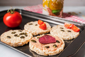 Crispy puffed rice cakes on table hummus spread and tomato and beet vegetables and sesame pumpkin seeds on the table - close up view on healthy vegetarian or vegan breakfast gluten free