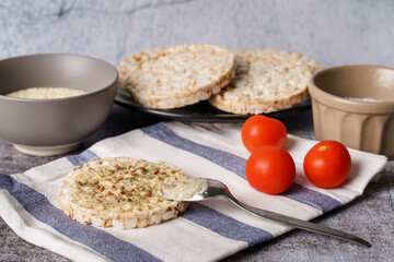 Crispy puffed rice cakes on table hummus spread and tomato vegetables and sesame seeds on the table - top view on healthy vegetarian or vegan breakfast gluten free copy space
