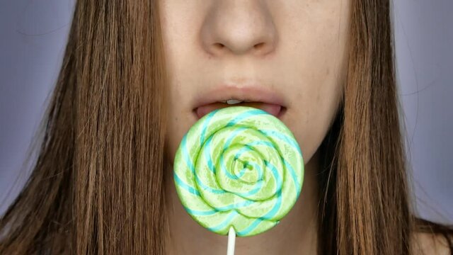Close-up of the girls lips licking a green-blue lollipop