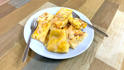 Ready-to-eat Roti, a flat bread, filled with egg and sliced banana and sweetend condensed milk, served on the light brown-colored table.