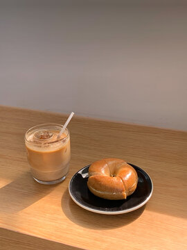 A Toasted Bagle in the blue plate and a cup of Iced Caffe Latte served on the wooden table.