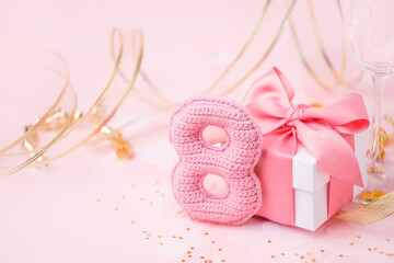 8 March, International Women's Day concept. Figure eight of pink crochet with luxury gift box, big bow on pink background. Space for text, monochrome seasonal holiday greeting card