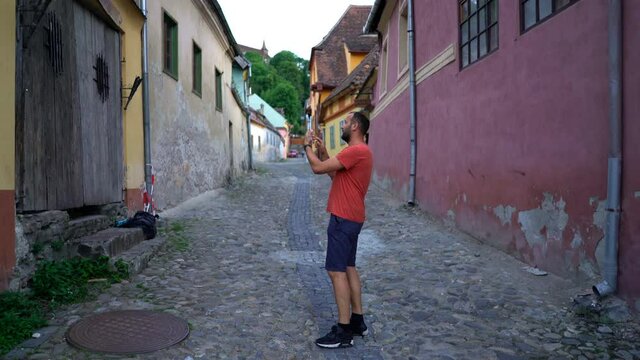 Young man taking photo of old town in Romania with tablet computer