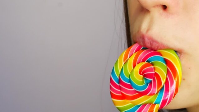 Close-up of a lower part of the face of young lady sucking a beautiful multicolored lollipop