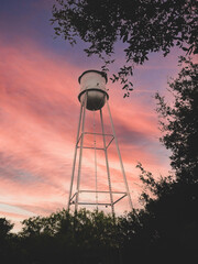 isolated Water tower against colorful sky with trees in foreground