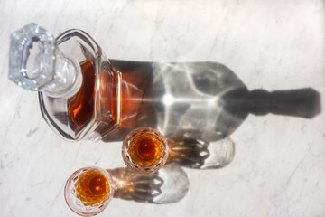 Whisky decanter and two glasses on a marble background top down view with shadows.
