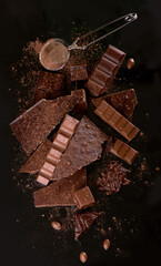 Broken chocolate pieces and cocoa powder on wooden background.