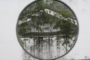 some thin green bamboos are seen through a round door among several old white buildings