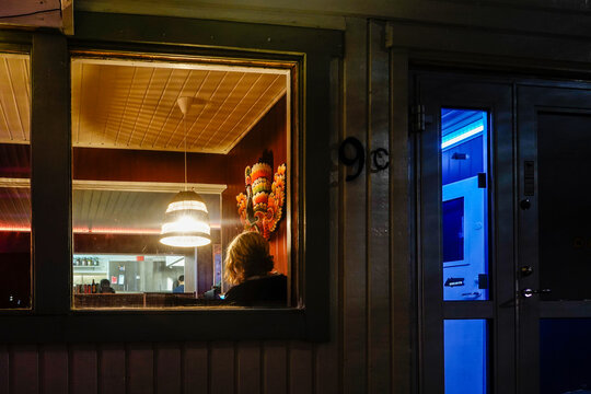 Stockholm, Sweden A Woman Sitting In The Window At Night  Of A Sri Lankan Restaurant In A Desolate Industrial Area.