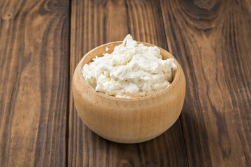 A large wooden bowl filled with homemade cottage cheese on a wooden table.