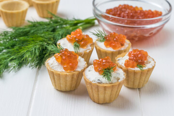 Tartlets with cream cheese and caviar on the background of a glass bowl with red caviar.