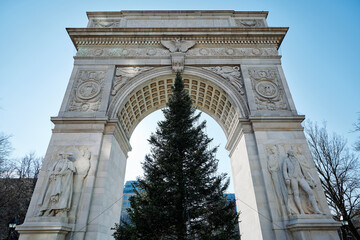 Fototapeta na wymiar wide angle view of Washington Square Arch and Chritsmas tree from ground up to clear blue sky. The Tuckahoe marble bas relief details show an eagle, two coats of arms and statues.