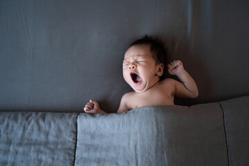 sleepy baby yawning. naked asian baby infant sleeping on gray bed with blanket. studio shot.