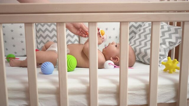 Newborn baby lies in the crib and plays with a rattle