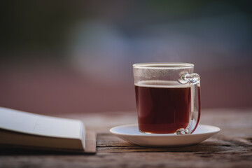 A cup of hot morning coffee on wooden table with a diary notebook at the balcony of the sleeping room to welcome sunshine in the morning, a glass of black coffee with a notebook on the wooden table