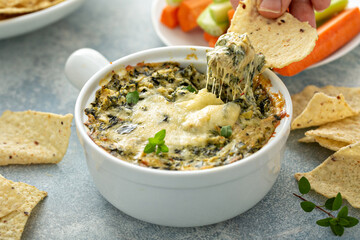 Artichoke spinach dip in a baking dish with a cheese pull - obrazy, fototapety, plakaty