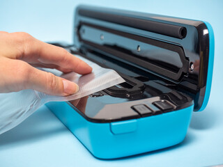 Blue vacuum cleaner for sealing packages on a blue background. The hand inserts the package into...