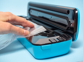 Blue vacuum cleaner for sealing packages on a blue background. The hand inserts the package into it. Selective Focus