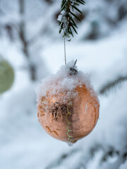 a shiny Christmas tree toy in the form of a ball hangs in the forest on a twig. Close-up, snow on a toy