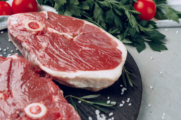 Raw rib-eye beef steak on wooden cutting board on gray background