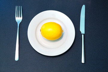 Yellow lemon on white plate with knife and fork.