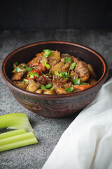 Stewed vegetables with spices in an earthen bowl on a dark gray slate or stone background. View from above.