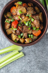 Stewed vegetables with spices in an earthen bowl on a dark gray slate or stone background. View from above.