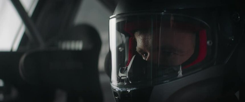 CU portrait of sports car driver closing helmet visor, starting a race on a speedway. Shot with 2x anamorphic lens