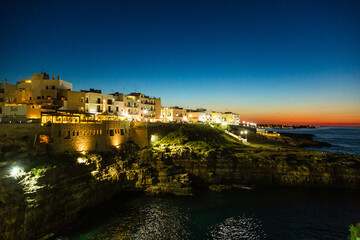 Obraz na płótnie Canvas イタリア　ポリニャーノ・ア・マーレの日没後のカラ・ポルト海岸と断崖の上の町並み