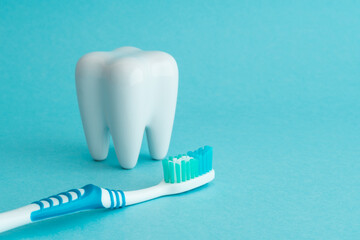 White healthy tooth model and blue dental toothbrush on blue background with copy space. Dental care and healthcare concept.