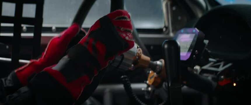 CU on hands and steering wheel, sports car driver in racing on a speedway. Fast speed, motorsport. Daytime shot. Shot with 2x anamorphic lens
