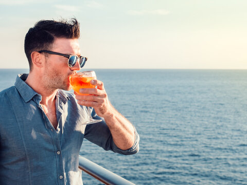 Handsome man and beautiful glass with a drink on the background of sea waves and sun rays. Close-up. Concept of leisure and travel