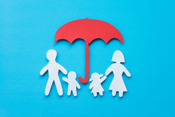 Life insurance concept. Paper cutout of family (father, mother, son and daughter) under red umbrella on blue background. Insurance is life planning for happy future.