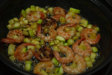 Diet vegetarian vegetable warm salad with king prawns, cherry tomatoes, avacado, zucchini, lime and aromatic herbs in a transparent glass bowl on a granite table.