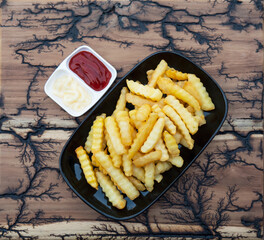 Top view of French fries with sauces on wood plate