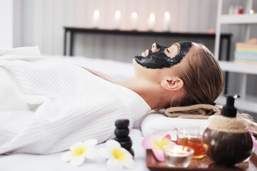 Obraz na płótnie Canvas Smiling Caucasian woman in white is laying on bed and black facial mask on face for treatment skine care at spa.